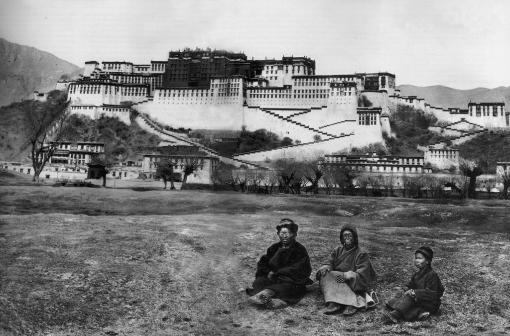 Alexandra in, dressed as a beggar and face covered in grease, Lama Yongden, and a young Tibetan pose upon the backdrop of the Potala Palace, in Lhasa, Tibet's capital, in 1924. © Archives Fondation Alexandra David-Néel — Ville de Digne-les-Bains (Click to view larger version...)